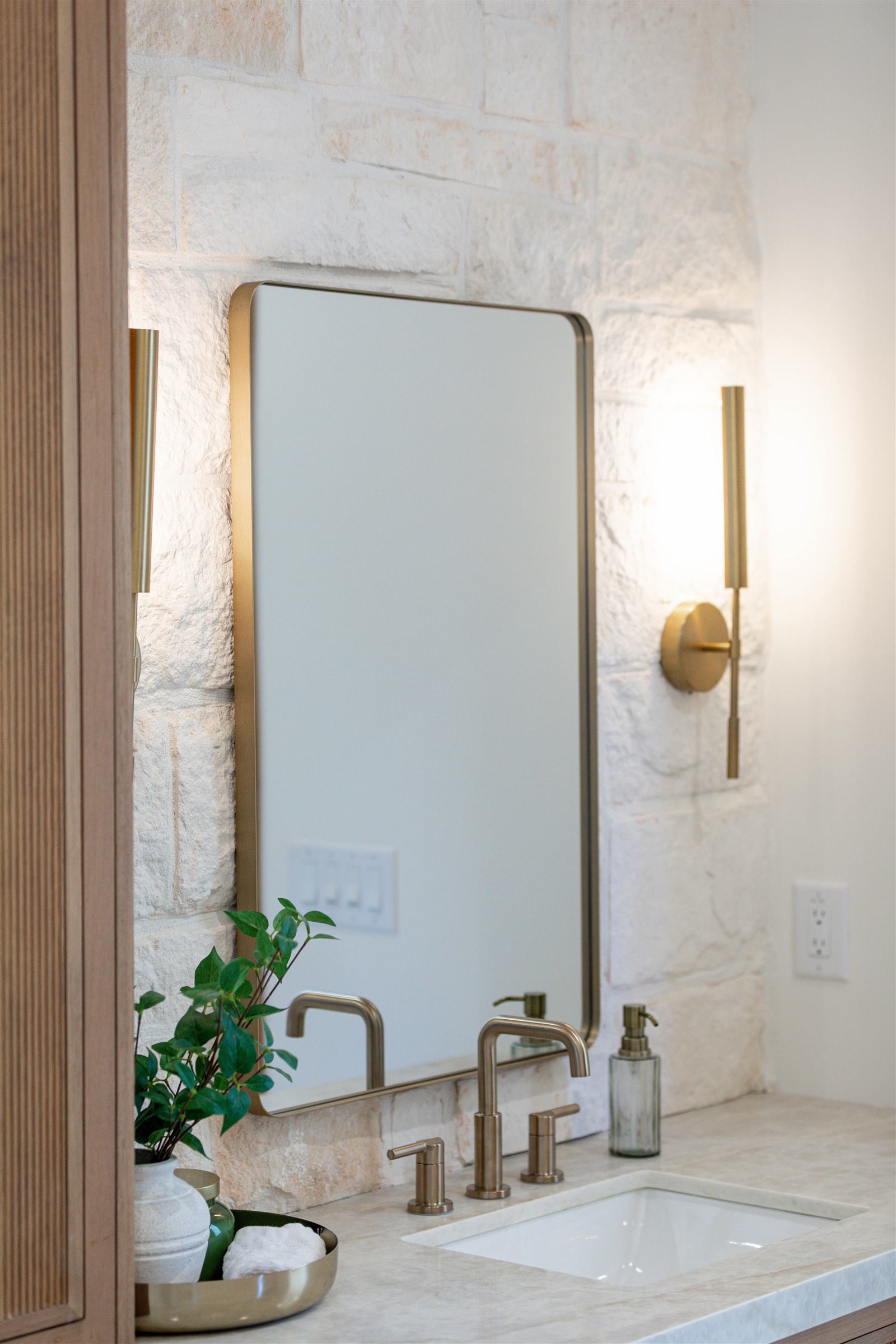 Primary bathroom vanity with stone backsplash and brass fixtures