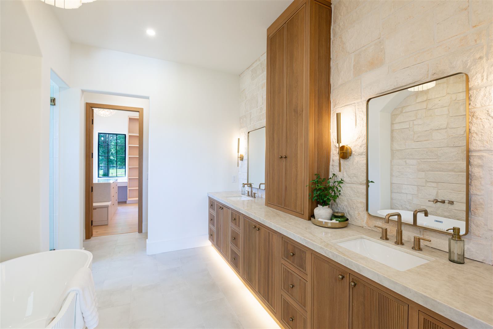 Primary bathroom with double vanity, stone accent wall, and freestanding tub